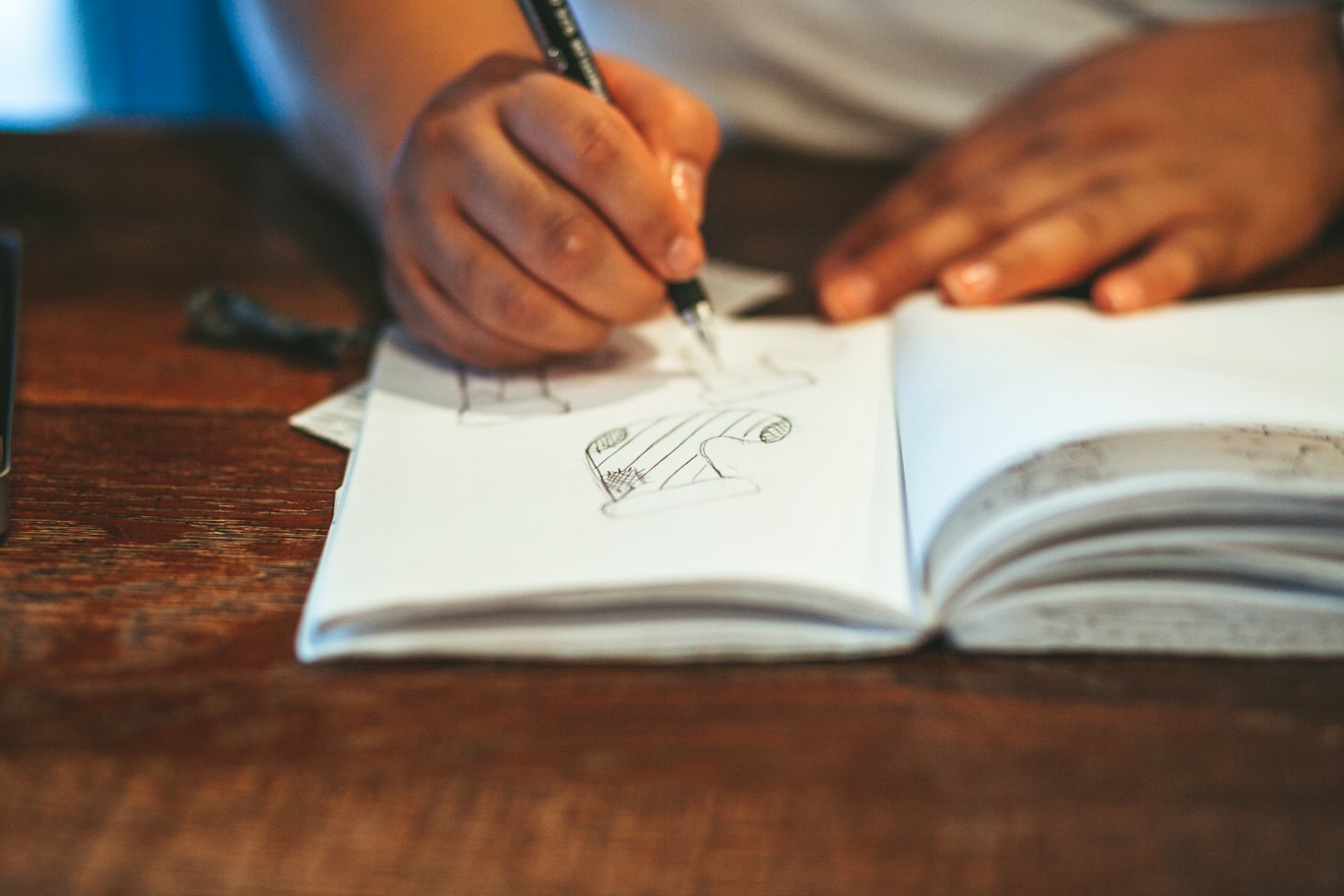 Hands use a mechanical pencil to sketch in a notebook.